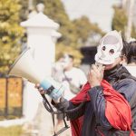 A masked protestor in West Java, Indonesia, using a megaphone during a daytime demonstration.